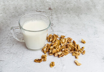 Organic walnut nuts and glass of walnut milk on gray  background