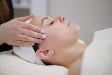 Obraz na płótnie Canvas Woman receiving head massage. Calm patient woman undergoing the cosmetic facial massage procedures for rejuvenation skin face