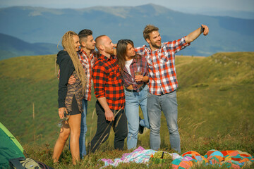 Group of friends taking a selfie in the mountains. Group of young people spend free time together, happy men with guitar and girls on camping.