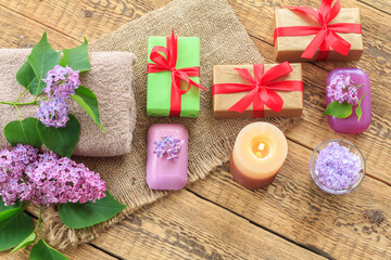 Towels, soap, gifts, candle and lilac flowers on wooden background.