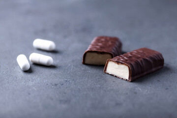 High Protein bar and creatine capsules. Bodybuilding food supplements on dark stone background. Close up. Copy space.