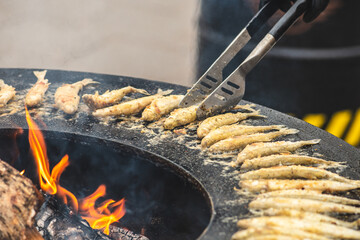 Preparing traditional tasty fried European smelt fish being cooked on an open fire in a street food...