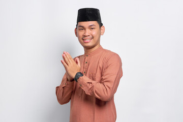 Smiling young Asian Muslim man gesturing Eid Mubarak greeting isolated over white background