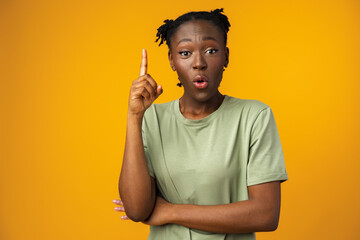 Cheerful Afro woman points to copy space in yellow studio