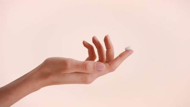 Close-up shot of a female hand with a drop of beauty cream on the top of the finger against beige background