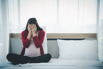 Pregnant woman sitting on bed and feeling upset and sad from family conflict problem.