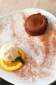 Close up of hot melting chocolate cake dessert and scoop of vanilla ice cream on orange slice on white plate. Chocolate fondant and ice cream. Top view, vertical photo.