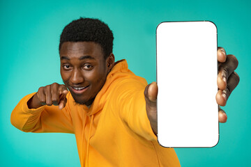 Smiling casual black man pointing at blank white cell phone screen in studio