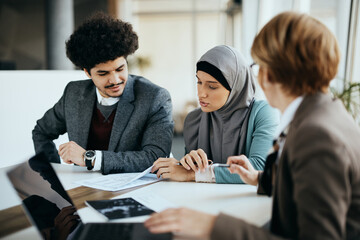 Young Muslim woman and her husband analyzing paperwork during meeting with their insurance agent.
