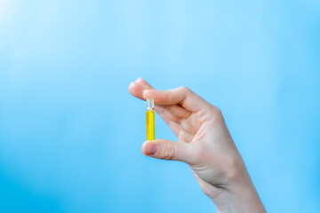 hand holding a vial of oil on a blue background