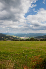 Obraz premium Vosges mountain landscape in the summer. The sky is overcast and a little blue. A large green meadow slopes down to the valley. In the distance another massif stands out.