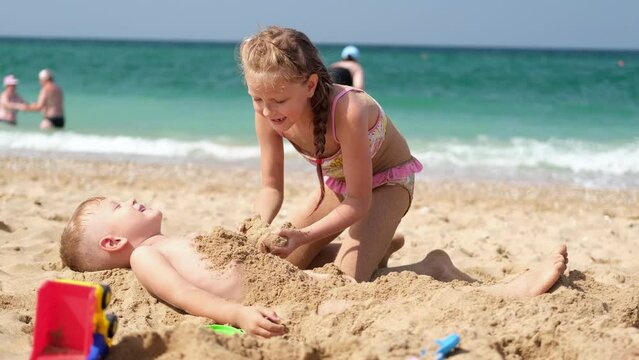 Brother and sister play in the sand on the beach. Children's games on the seashore. Rest, vacation.