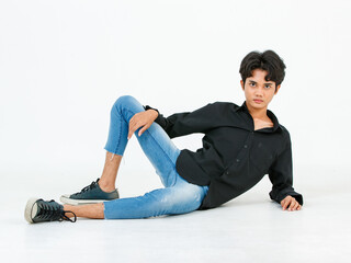 Portrait isolated cutout studio shot of Asian young LGBTQ gay glamour male model in casual black shirt and jeans outfit sitting stretching posing gesturing on floor look at camera on white background