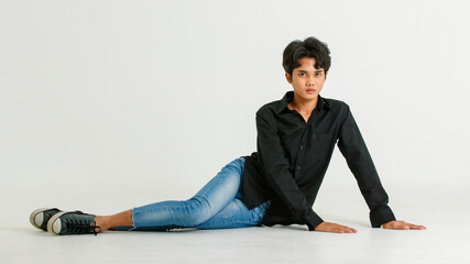 Portrait isolated cutout studio shot of Asian young LGBTQ gay glamour male model in casual black shirt and jeans outfit sitting stretching posing gesturing on floor look at camera on white background