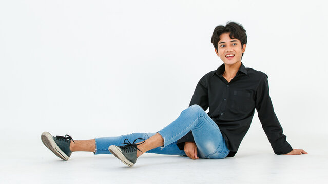 Portrait isolated cutout studio shot of Asian young LGBTQ gay glamour male model in casual black shirt and jeans outfit sitting stretching posing gesturing on floor look at camera on white background