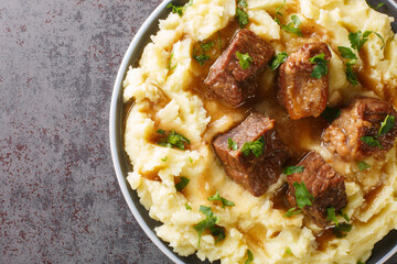 Slowly stewed beef with wine and vinegar garnished with mashed potatoes close-up in a plate on the table. horizontal top view from above