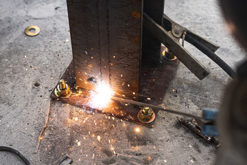 A welder is welding and installing a steel column structure on a steel plate.