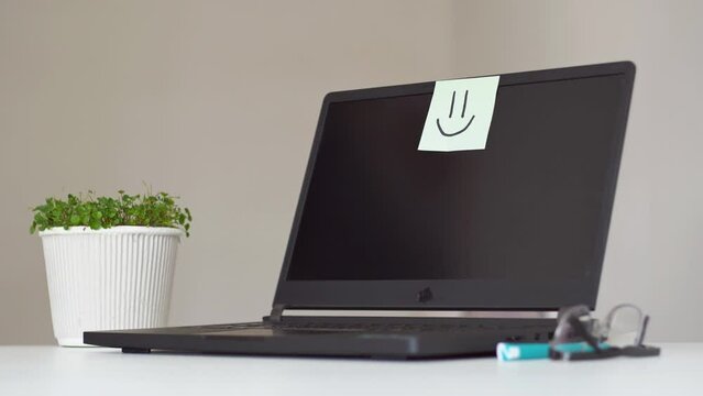 Good working environment and happy atmosphere in workplace. Team spirit. Smiley face drawn on a sticky paper and post it note on laptop in office.