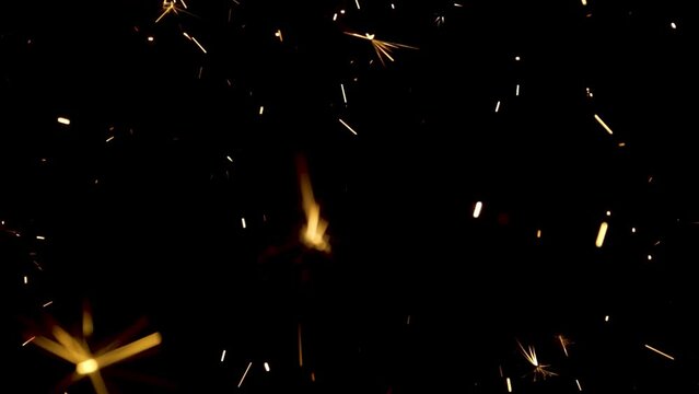 Sparkling splashes of bengal fires on black background. Lightening shine particles sparkler in dark. Sparkling bengali firework with golden splashes of sparks. Concept holiday. Close up. Slow motion.