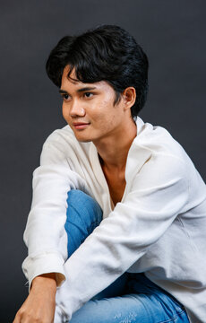 Studio closeup shot of Asian young LGBTQ gay glamour happy handsome bisexual homosexual male fashion model in casual long sleeve shirt outfit sitting smiling posing gesturing on black background