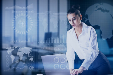 Attractive young european woman using laptop at desktop with abstract global digital business interface on blurry background. Accounting, chart, finance and hud concept. Double exposure.