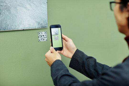 Unrecognizable young man spending time in modern art gallery scanning QR code using his smartphone to get more information about photo on wall