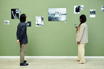Horizontal wide shot of young Asian man and Black woman spending free time visiting modern black and white photography exhibition in art gallery
