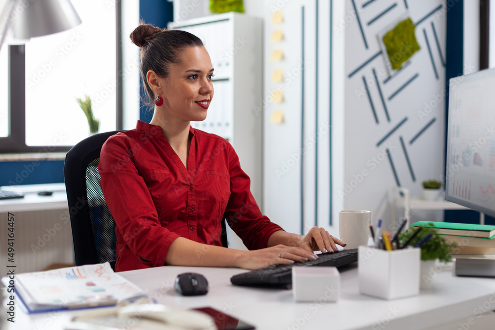 Poster smiling startup owner looking at computer monitor typing on keyboard. small business manager in red 