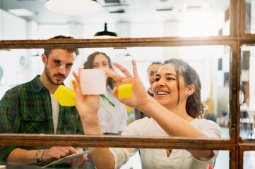 Shot through the window of Group of young team workers writing on post stickers at office glass. Business, startup and planning concept.