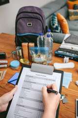 Unrecognizable woman doing checklist of emergency backpack in the living room