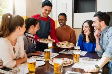 Foto op Canvas Multiracial group of friends sitting at table restaurant looking hungry the pizzas that the waiter is bringing. © Pintau Studio
