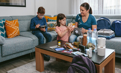 Mother preparing emergency backpack with her children in the living room