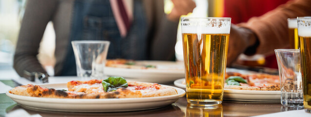 Vertical Close-up glass of beer with froth on table next to a plate with Margherita pizza....