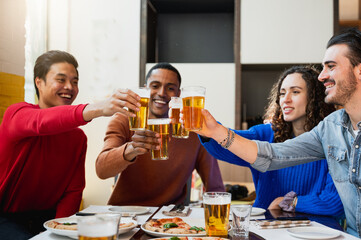 Group for young people sitting at table in a restaurant. Friends are celebrating with glass of beer.