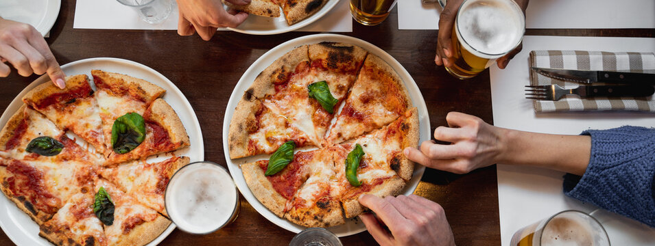 Horizontal banner or header Top view table with unrecognizable multiracial group of people's hands grabbing a slice of delicious Italian pizza and glasses of beer