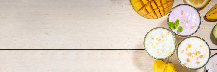 Refreshing yogurt, milkshakes or smoothies. Three glasses with fruit milkshakes. White banana, green apple avocado, yellow mango tropical fruits smoothie. On white wooden table, copy space