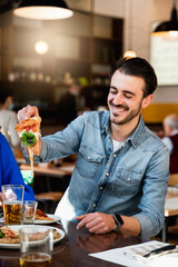 Vertical shot young hipster caucasian man sitting at table in restaurant laughing because his piece of pizza has stringy cheese.