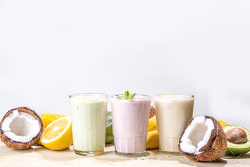 Refreshing yogurt, milkshakes or smoothies. Three glasses with fruit milkshakes. White banana, green apple avocado, yellow mango tropical fruits smoothie. On white wooden table, copy space