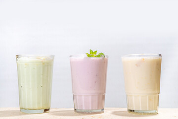 Refreshing yogurt, milkshakes or smoothies. Three glasses with fruit milkshakes. White banana, green apple avocado, yellow mango tropical fruits smoothie. On white wooden table, copy space