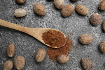 Spoon of nutmeg powder and seeds on grey table, flat lay