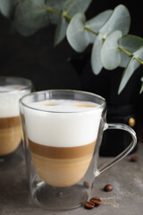 Glass cups of delicious latte macchiato and scattered coffee beans on grey table