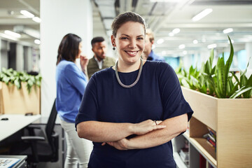 Here to become the best. Portrait of a young designer standing in an office with her colleagues in the background.