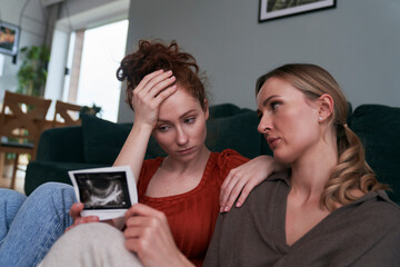 Woman holding ultrasound scan and being consoled by the best friend