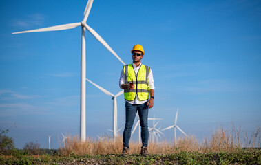 Engineer wearing uniform ,helmet hold document inspection work in wind turbine farms rotation to generate electricity energy. Green ecological power energy generation wind sustainable energy concept.