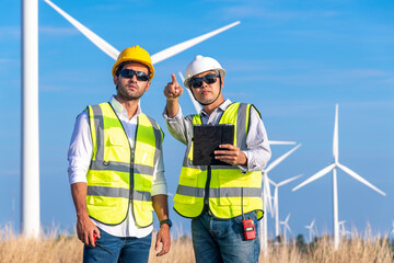 Engineer wearing uniform ,helmet hold document inspection work in wind turbine farms rotation to generate electricity energy. Green ecological power energy generation wind sustainable energy concept.