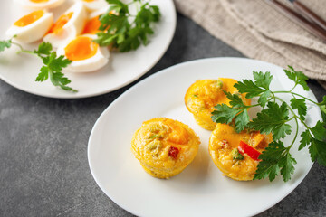 Boiled eggs and Egg muffins ( bites) with parsley leaves  in a plate on a gray background.