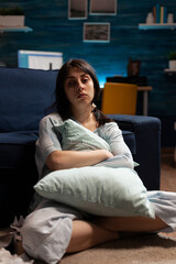 Obraz premium Portrait of depressed woman with mental health problems sitting on floor and hugging pillow in living room. Anxious sad person dealing with chronic disease difficulties and depression at home.
