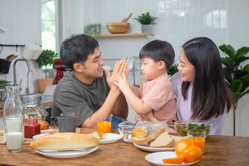 Asian family breakfast at happy home. Parents and children enjoy eating together, talking with laughter and good atmosphere. Father plays with son playfully at kitchen table