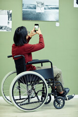 Unrecognizable Asian man with disability visiting exhibition in modern art gallery scanning QR code...