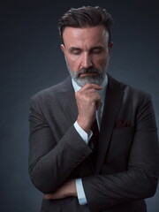 Portrait of a stylish elegant senior businessman with a beard and casual business clothes in photo studio isolated on dark background gesturing with hands